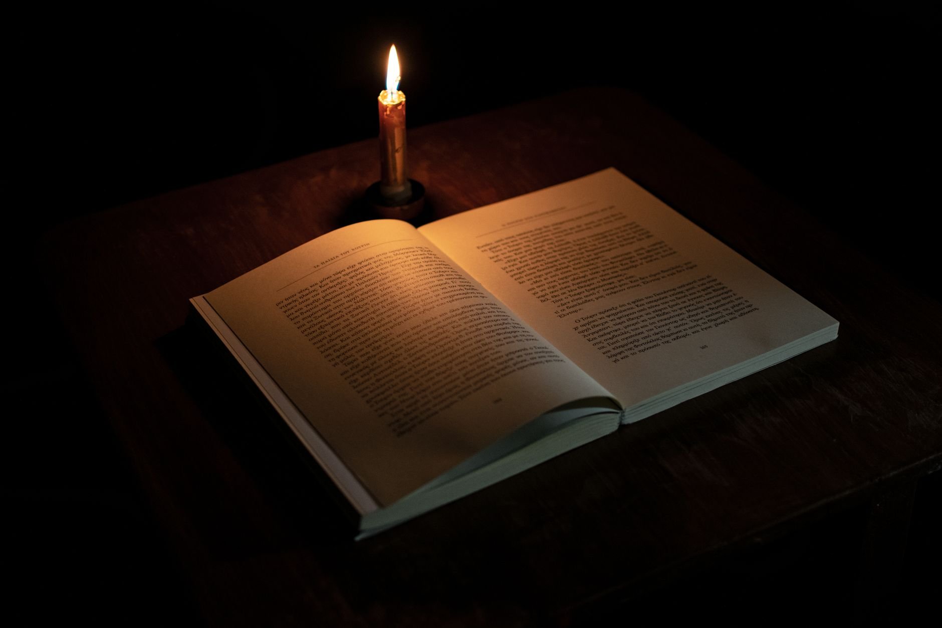 An open book illuminated by candlelight on a wooden table, creating a warm, cozy atmosphere.